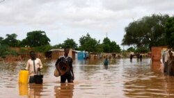 Des gens, portant leurs effets personnels, marchent dans une rue inondée du quartier Kirkissoye à Niamey, au Niger, le 27 août 2020.