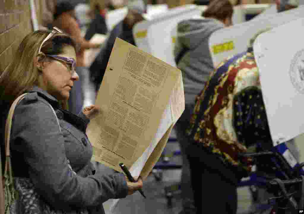 Because all the privacy booths are full, Miriam Rodriguez looks over her ballot while leaning against the wall at a polling site in New York, Nov. 4, 2014. 