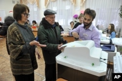 Members of an election commission help a man, center, to cast his ballot in the presidential election in Yekaterinburg, Russia, Sunday, March 18, 2018.