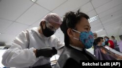 In this Tuesday, April 28, 2020, photo, Pornsupa Hattayong gives haircuts to a medical worker treating COVID-19 patients at Bangkok Metropolitan Administration General Hospital in Bangkok, Thailand. 