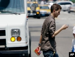 FILE - A man crosses a street in downtown Chicago while checking his phone.