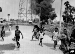FILE-Children run from burning buildings set on fire by rocket attacks near Phnom Penh Airport in Cambodia, the day the city was taken by Khmer Rouge troops, April 17, 1975. (AP Photo)