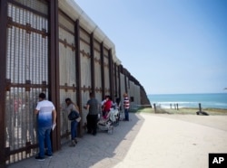 n this May 1, 2016 picture, Eva Lara, second from let, reacts as she reaches for her grandmother Juana Lara through the border wall during a brief visitation near where Mexico and the United States meet at the Pacific Ocean in San Diego.