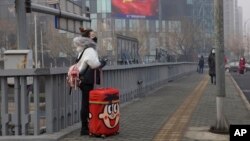 អ្នក​ដំណើរ​ឈរ​នៅ​លើ​ស្ពាន​ជិត​ផ្លាក​ឃោសនា​របស់​រដ្ឋាភិបាល ដែល​បង្ហាញ​អំពី​ការ​ប្រយុទ្ធ​ប្រឆាំង​នឹង​មេរោគ Covid-19 នៅ​ទីក្រុង​ប៉េកាំង ប្រទេស​ចិន។