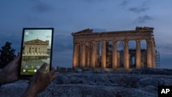 A man holds up a tablet showing a digitally overlayed virtual reconstruction of the ancient Parthenon temple, at the Acropolis Hill in Athens, Greece on Tuesday, June 13, 2023. (AP Photo/Petros Giannakouris)