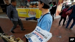 A vendor gives out copies of newspaper with a headlines of "Wuhan break out a new type of coronavirus, Hong Kong prevent SARS repeat" at a street in Hong Kong, Saturday, Jan. 11, 2020. (AP Photo/Andy Wong)