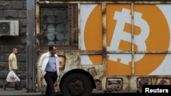 Des gens passent devant un panneau portant le logo de Bitcoin dans une rue d'Erevan, en Arménie, le 9 septembre 2019. (REUTERS/Anton Vaganov)