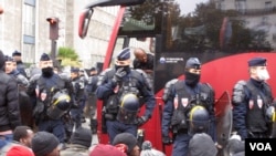 Des migrants attendent un bus devant des policiers à Paris, France, novembre 2016. . (VOA / L. Bryant)