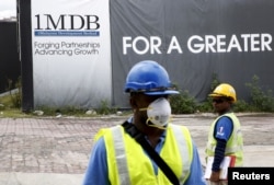 FILE - Construction workers stand in front of a 1Malaysia Development Berhad (1MDB) billboard at the Tun Razak Exchange development in Kuala Lumpur, Malaysia.