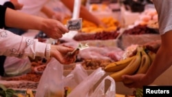 FILE - Customers pay money as they purchase bananas at a market in Beijing, China.