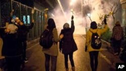 In this photograph taken Saturday, Jan. 11, 2020, protesters hold flowers as tear gas fired by police rises at a demonstration in front of Amir Kabir University in Tehran, Iran.
