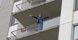 An apartment resident cheers her neighbors on as they sing and dance to lift the community's spirits while in isolation, Bethesda, Maryland.