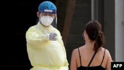 A medic wearing personal protective equipment (PPE) gestures to a woman waiting to take a Covid-19 coronavirus test at the National Olympic Stadium in Phnom Penh on February 23, 2021. (Photo by TANG CHHIN Sothy / AFP)