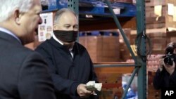 Washington Gov. Jay Inslee empties his wallet of cash to hand over to an official after Lakewood Mayor Don Anderson, left, handed over his paycheck in response to the coronavirus outbreak April 3, 2020, in Lakewood, Wash.