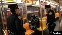 Pripadnici njujorške politicje bude putnika u vozu njujorškog metroa. Podzemna železnica je, prvi put u istoriji, planski zatvorena zbog detaljnog čišćenja, 6. maja 2020. 