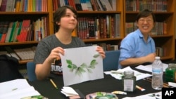 Undergraduate student Moe Lewis, left, shows her watercolor painting of peony leaves at a traditional Chinese painting class at the Confucius Institute at George Mason University in Fairfax, Va., on May 2, 2018. (AP Photo/Matthew Pennington)