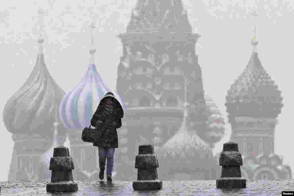 A woman walks along Red Square under snowfall, with St. Basil's Cathedral seen in the background, in central Moscow, Russia.
