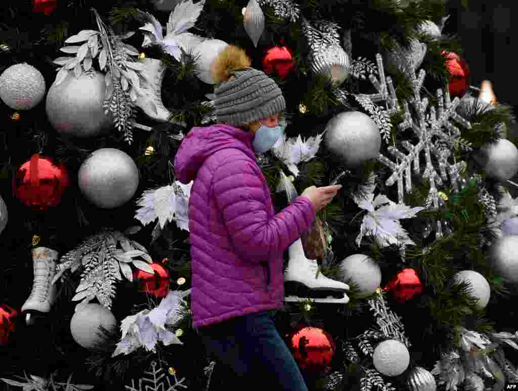 Una mujer con una mascarilla pasa junto a un árbol de Navidad decorado en medio de la pandemia de COVID-19 en Arlington, Virginia, el 18 de diciembre de 2020. [AFP]