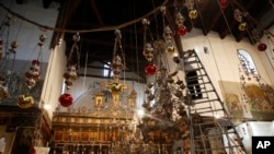 In this Wednesday, Dec. 5, 2018 photo, a worker cleans the dust from a chandelier at the Church of the Nativity, built atop the site where Christians believe Jesus Christ was born, in the West Bank City of Bethlehem. (AP Photo/Majdi Mohammed)