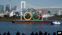 FILE - The Olympic Rings is put back up after they were taken down for repairs ahead of the postponed Tokyo 2020 Olympics in the Odaiba section of Tokyo, Tuesday, Dec. 1, 2020. (AP Photo/Eugene Hoshiko)
