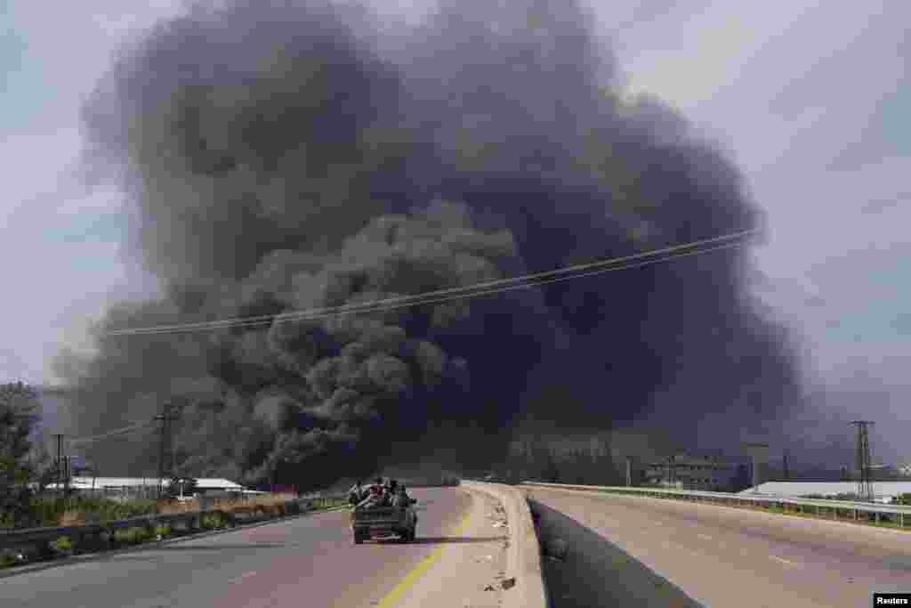 Smoke rises while members of the Syrian forces ride on a vehicle as they battle against a nascent insurgency by fighters from ousted leader Bashar al-Assad's Alawite sect, in Latakia, Syria.