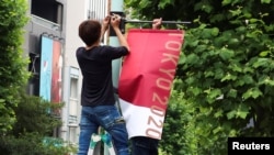 Workers attach the Tokyo 2020 Olympic Games banner on a lamp post in Tokyo, Japan, June 16, 2021. 