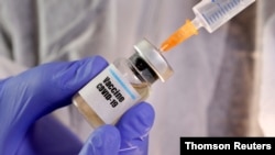FILE - A woman holds a small bottle labeled with a "Vaccine COVID-19" sticker and a medical syringe in this illustration.