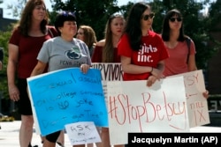 FILE - Sonja Breda, 23, right, holds a sign saying "Stop Betsy" as a group of survivors of sexual violence and their supporters gather to protest proposed changes to Title IX before a speech by Education Secretary Betsy DeVos at George Mason University, Sept. 7, 2017.