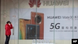 疫情期间一名妇女站在位于北京的华为手机5G广告旁。（2020年3月8日）