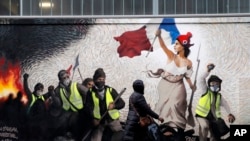 A woman passes by a mural by street artist PBOY depicting Yellow Vest (gilets jaunes) protesters inspired by a painting by Eugene Delacroix, "La Liberte guidant le Peuple" (Liberty Leading the People), in Paris, Jan. 10, 2019.