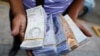 El asistente de un conductor de autobús sostiene billetes de Bolívar, por valor de entre 0,01 y 0,25 dólares estadounidenses, luego de que el Banco Central de Venezuela anunciara que recortará seis ceros de precios, en Caracas.