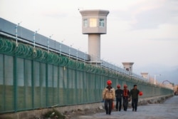 FILE - Workers walk by the perimeter fence of what is officially known as a vocational skills education center in Dabancheng in Xinjiang Uighur Autonomous Region, China,Sept. 4, 2018.