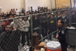 FILE - Men stand in a U.S. Immigration and Border Enforcement detention center in McAllen, Texas, July 12, 2019.