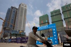 បុរសម្នាក់កំពុងជិះម៉ូតូកាត់ការដ្ឋានសាងសង់អគារមួយកន្លែងក្នុងតំបន់កោះពេជ្រ រាជធានីភ្នំពេញ កាលពីខែឧសភា ឆ្នាំ២០១៩។ (កាន់ វិច្ឆិកា/VOA)