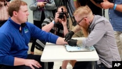 Tony Danna, left, vice president of international development at Three Square Market in River Falls, Wis., receives a microchip in his left hand at company headquarters, Aug. 1, 2017. (AP Photos/Jeff Baenen)