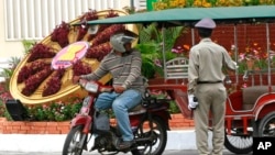 FILE PHOTO - A Cambodian police officer, right, talks with a motorcycle taxi driver next to a floral decoration set up ahead of the ASEAN Summit along a road in Phnom Penh, Cambodia, Sunday, April 1, 2012. 