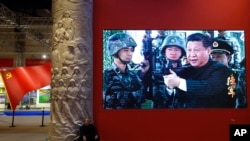 2017年10月23日，一名男子在北京的一個視頻屏幕旁邊休息。視頻顯示，中國國家主席習近平在北京展覽館舉行的一場展覽上拿著一支步槍。（美聯社照片）