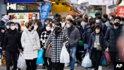Personas con bolsas de compras cruzan una intersección de tráfico hacia una estación de tren cerca de una calle comercial en el distrito de Ueno, famoso por las compras de fin de año antes de las vacaciones de Año Nuevo en Tokio, el viernes 30 de diciembre de 2022.