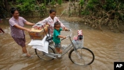 Villagers carried their government donation gift through a flooded street during its season near the Mekong River bank, northeastern Phnom Penh, Cambodia, Saturday, Aug. 18, 2018. (AP Photo/Heng Sinith)