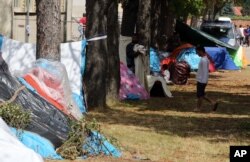 FILE - A refugee walks near tents at the refugee camp in Traiskirchen, Austria, July 31, 2015.