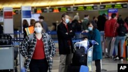 Travelers cover their faces with masks as they wait to drop their luggage at the Los Angeles International Airport Saturday, March 14, 2020, in Los Angeles. The coronavirus outbreak is hitting the airline industry hard. President Trump banned most…