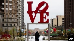 A person wearing a protective face mask and gloves as a precaution against the coronavirus walks by the Robert Indiana sculpture "LOVE" at John F. Kennedy Plaza, commonly known as Love Park, in Philadelphia, Monday, April 13, 2020. (AP Photo/Matt Rourke)