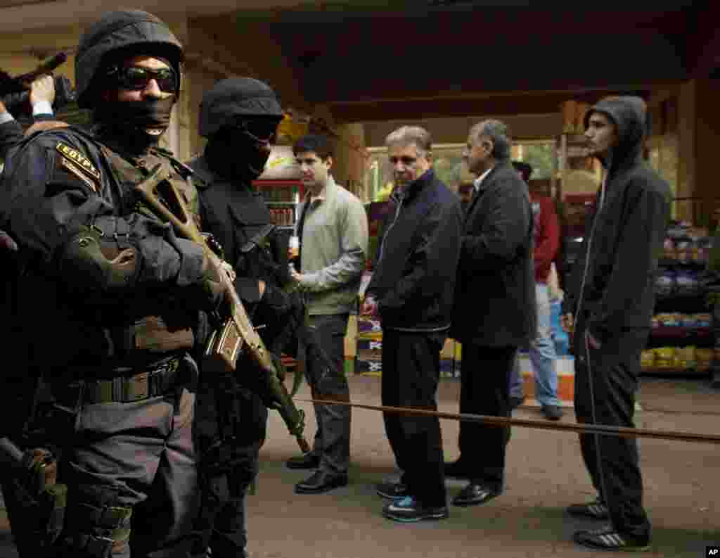 Members of the Egyptian Interior Minister's security detail stand guard as voters line up at a polling station on the first day of voting in the country's constitutional referendum in the Zamalek neighborhood in Cairo, Jan. 14, 2014. 