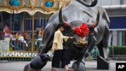 一名婦女在北京一家零售和批發服裝商場外面銅牛雕塑旁。 (2018年7月9日)