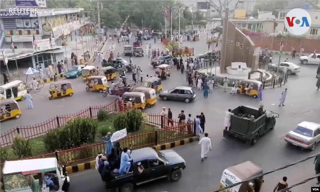 Militantes talibanes ondeando una bandera talibán en la parte trasera de una camioneta pasan por una calle concurrida en el área de la plaza Pashtunistan en Jalalabad, Afganistán. 