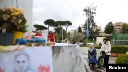 La gente reza junto a la estatua del difunto Papa Juan Pablo II afuera del Hospital Gemelli, donde el Papa Francisco está ingresado para recibir tratamiento por neumonía, en Roma, Italia, el 13 de marzo de 2025.