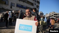 یک مرد فلسطینی یک بسته کمکی را حمل می‌کند که آنروا پس از آتش‌بس بین اسرائیل و حماس، در خان یونس در جنوب نوار غزه عرضه کرده است. ۲ بهمن ۱۴۰۳