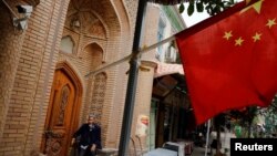 រូបឯកសារ៖ បុរស​ចំណាស់​ម្នាក់​កំពុង​អង្គុយ​នៅ​ក្បែរ​ទង់​ជាតិ​ចិន​នៅ​ទីក្រុង​ចំណាស់​នៃ​ក្រុង Kashgar តំបន់​ស្វយ័ត Xinjiang Uighur ប្រទេស​ចិន កាល​ពី​ឆ្នាំ​២០១៨។