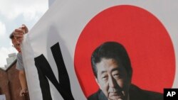 A South Korean man stands next to a sign with a picture of the Japanese Prime Minister Shinzo Abe during a rally to denounce Japan's trade restrictions on South Korea in Seoul, South Korea, Aug. 8, 2019.