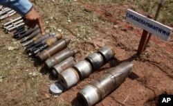 FILE - A Cambodian demining expert points to unexploded bombs displayed on the ground before a destruction ceremony organized by the Cambodia Mine Action Center (CMAC) at the complex of the Preah Vihear temple in Preah Vihear province, about 245 kilometers (152 miles) north of Phnom Penh, July 7, 2011.